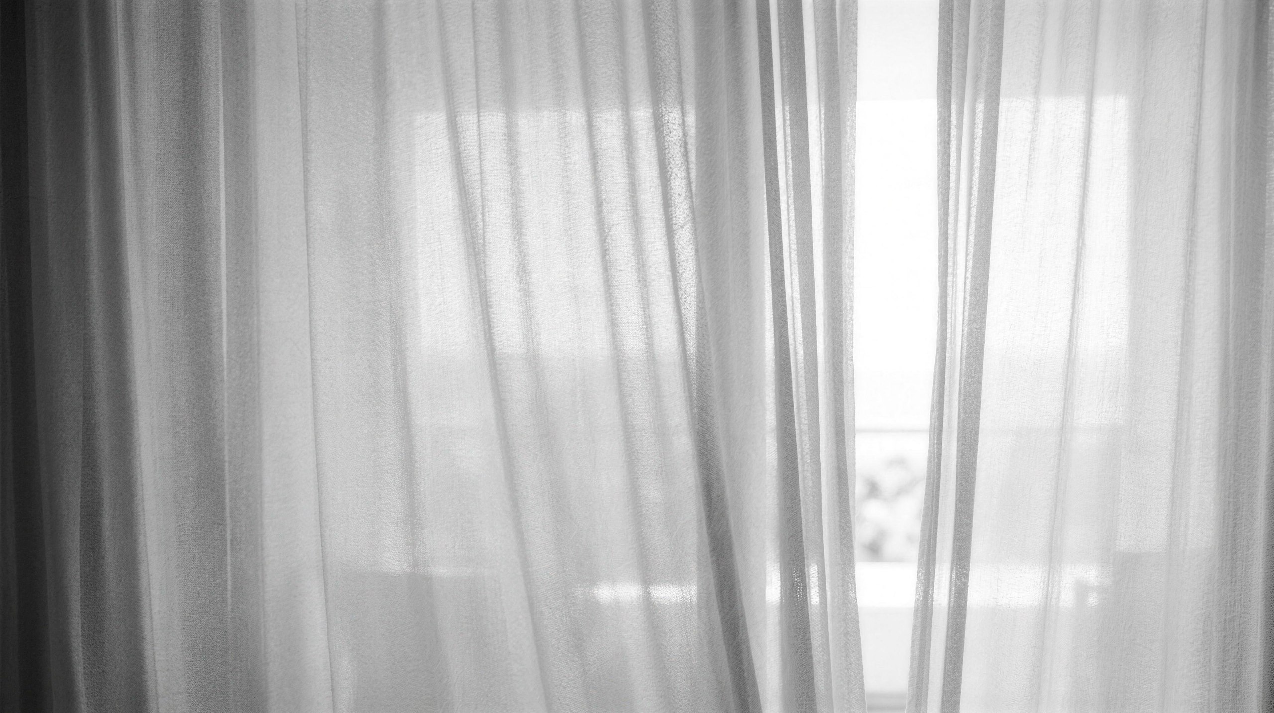 Sheer linen curtains parting on a seam of bright daylight.
